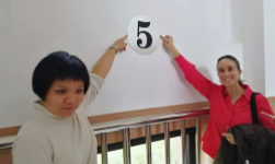 Zhan Ge and Helen pointing to a number five written on a wall.