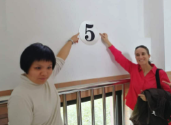 Zhan Ge and Helen pointing to a number five written on a wall.