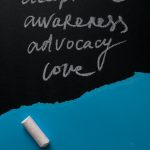Four words written in chalk on a black board acceptance, awareness, advocacy, love.